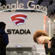 A photo shows two people looking at a Stadia controller with a large Google logo behind them.